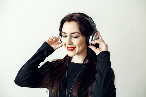 Happy pretty smiling woman with red lips in a black jacket listens to music  - Foto, Bild