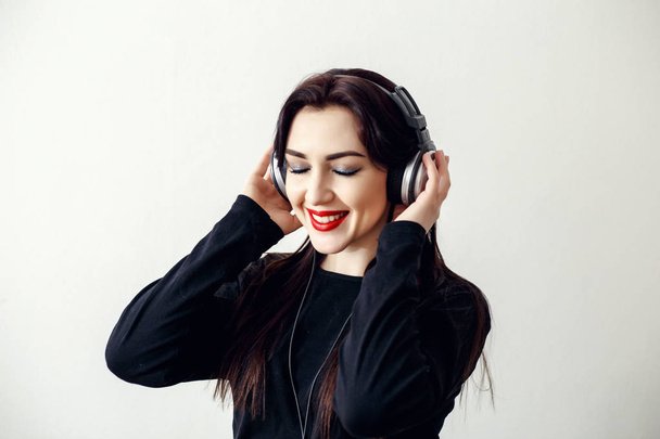 Happy pretty smiling woman with red lips in a black jacket listens to music  - 写真・画像