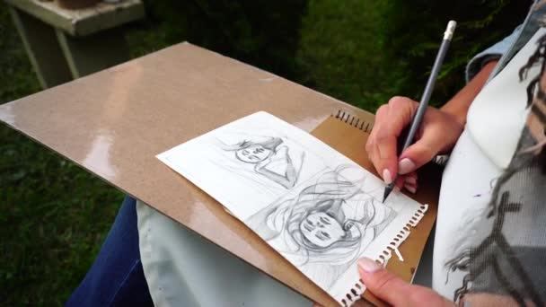 Hand van meisje kunstenaar maakt zeker scherp potlood lijnen op de albumpagina's, die toont schets portret van onbekende meisje. Master zit in Park in openlucht. - Video