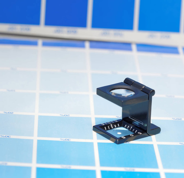 Magnifier or printer's loupe sits on a cyan test sheet - Photo, Image