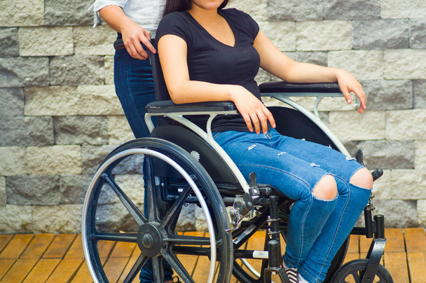 Young woman sitting in wheelchair with assistant standing next to her, both smiling happily showing positive attitude, physical recovery concept - Zdjęcie, obraz
