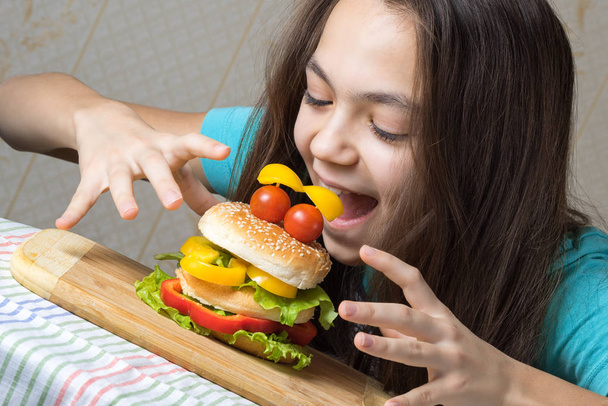 Retrato de uma menina de 11 anos, um hambúrguer comendo como um rosto sorridente com olhos de tomate
 - Foto, Imagem