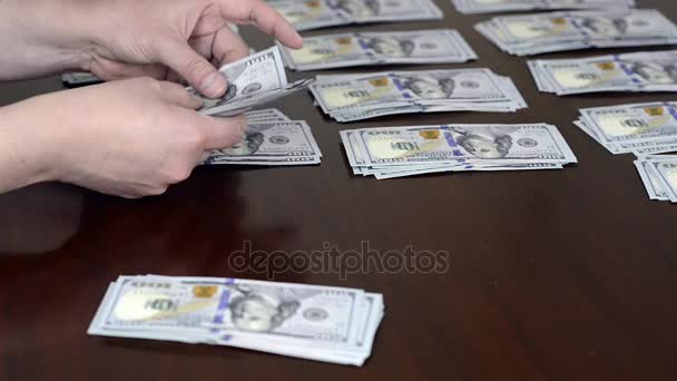 Мужские руки подсчитывают и укладывают деньги в банкноты по сто долларов на рабочем столе
 - Кадры, видео