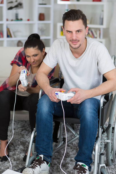 young couple playing video games at home boyfriend in wheelchair - Photo, Image