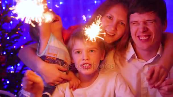 Šťastná rodina zapálil prskavky na večírku. V pozadí, bokeh světla a girlandy vánoční jedle - Záběry, video