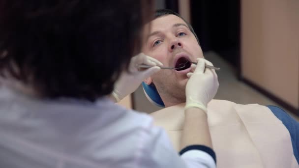female dentist making procedures to male patient at clinic, close up - Materiał filmowy, wideo