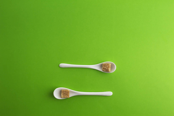 Two white spoons with brown sugar cubes on greenery background. Top view. Copy space for text. - Фото, зображення