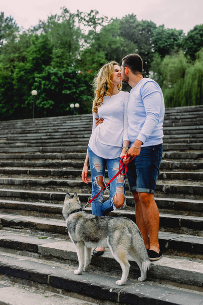 Beautiful young couple playing with a dog husky in a park. Summe - Photo, Image
