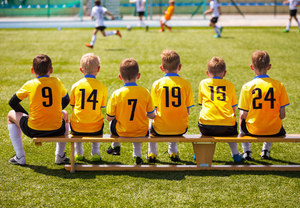 Young Football Players. Young Soccer Team Sitting on Wooden Bench. Soccer Match For Children. Young Boys Playing Tournament Soccer Match. Youth Soccer Club Footballers - Foto, Imagen