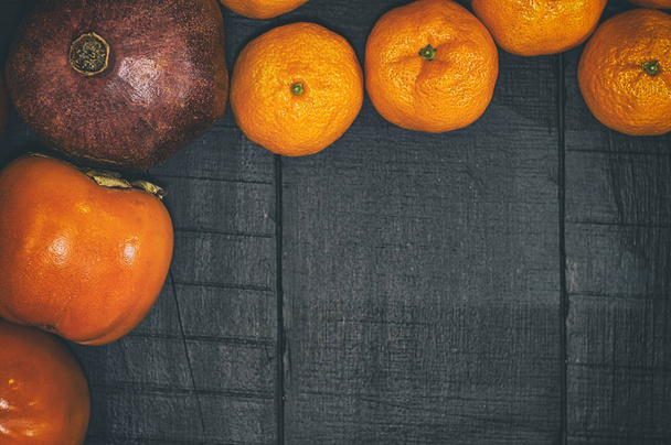 Mandarinas, granada y caqui sobre una superficie de madera negra
 - Foto, imagen