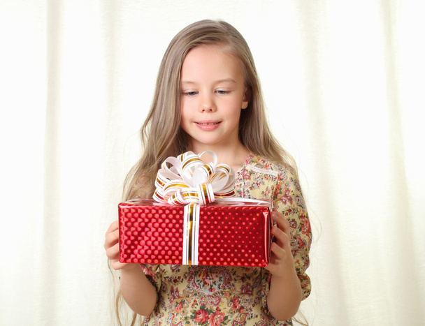 Little blond girl holding a red glamorous gift with pleasure - Foto, Bild