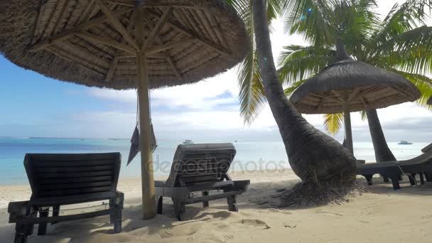 Vista de la chaise-longue vacía cerca de sombrilla nativa y palmeras contra el agua azul, Isla Mauricio - Metraje, vídeo