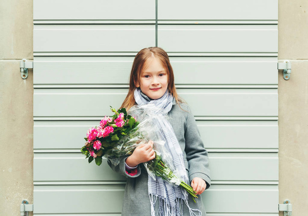 Outdoor portrait of 5-6 year old little girl wearing grey coat and scarf, holding bouquet of pink roses - Foto, afbeelding