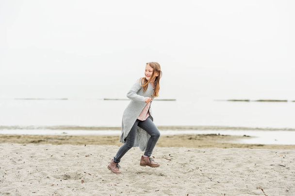 Adorable niña de 8-9 años jugando junto al lago, vistiendo pantalones grises y un largo cárdigan
 - Foto, imagen