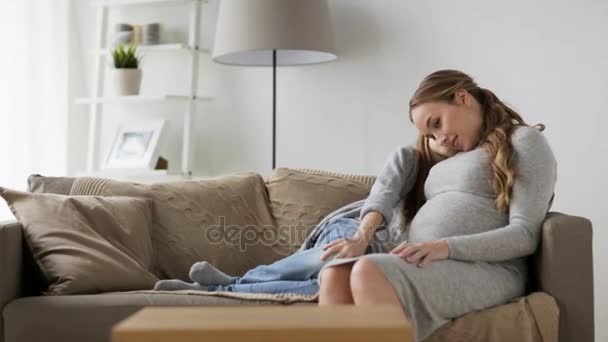 happy pregnant woman and girl on sofa at home - Materiał filmowy, wideo