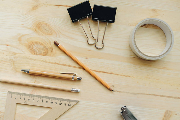 Деревянный карандаш, ручка, треугольник, скрепки для бумаг, обойма на столе при дневном свете. Офисный стол
 - Фото, изображение