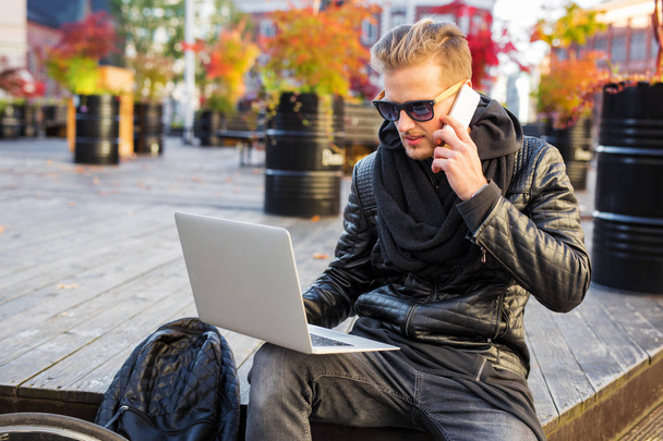 Hipster hombre en la ciudad trabajando en el ordenador portátil y hablando por teléfono
 - Foto, imagen