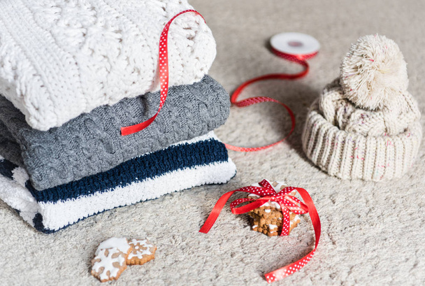 Pilha de roupas de inverno de malha e biscoitos decorados com fita vermelha
 - Foto, Imagem