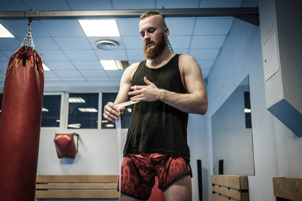 Combatiente preparándose para el entrenamiento, envolviendo las manos con envolturas de boxeo
 - Foto, Imagen