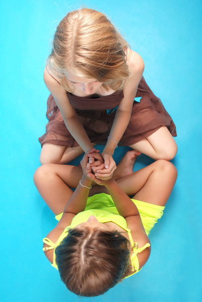 Dziewczyny, trzymając się za ręce siedzący na niebieskim tle - Zdjęcie, obraz
