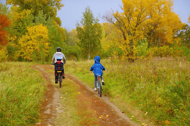 Family on bikes in golden autumn park, father and kids cycling on trail, active sport with children outdoors - Valokuva, kuva