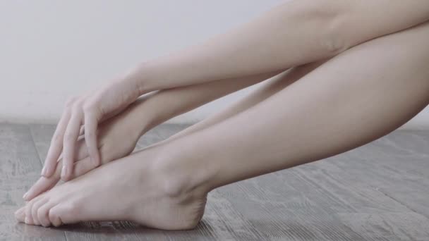 Κορίτσι αγγίζοντας απαλά τα πόδια της να κάθεται στο ξύλινο πάτωμα με λευκό τοίχο στο φόντο. - Πλάνα, βίντεο