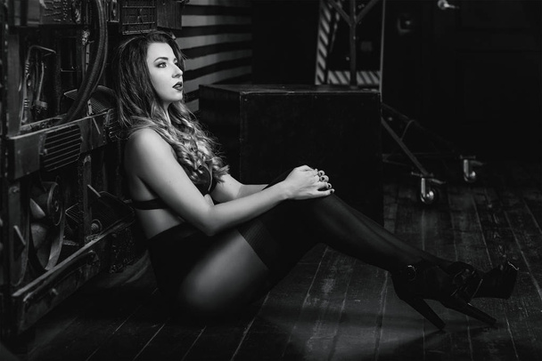 junge schöne attraktive und heiße langhaarige Frau in schwarzer Unterwäsche auf industriellem Hintergrund im Fotostudio monochrom  - Foto, Bild