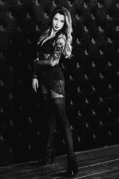 Nuori kaunis houkutteleva ja kuuma pitkät hiukset nainen mustissa alusvaatteissa lähellä mustaa samettiseinää valokuvastudiossa
 - Valokuva, kuva