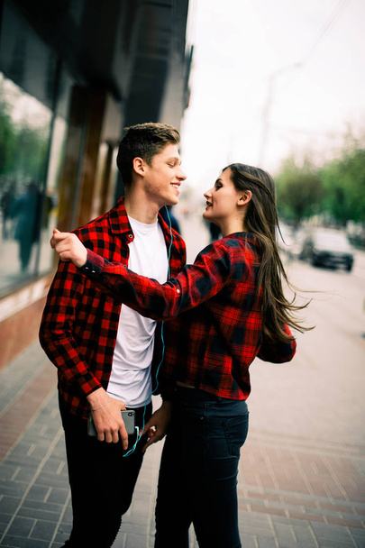 Two happy trendy teenage friends walking and dancing in the city, listening to the music with headphones, talking each other and smiling. Lifestyle, friendship and urban life concepts. - Zdjęcie, obraz