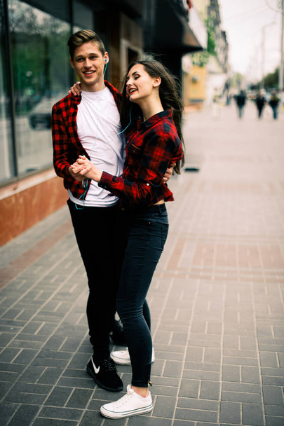 Two happy trendy teenage friends walking and dancing in the city, listening to the music with headphones, talking each other and smiling. Lifestyle, friendship and urban life concepts. - Φωτογραφία, εικόνα