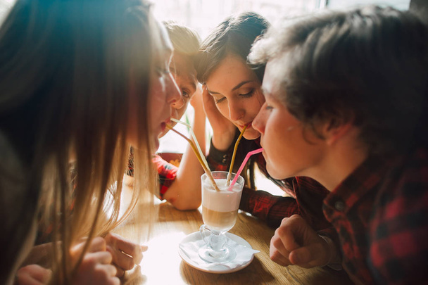 Un grupo de jóvenes amigos pasando el rato en una cafetería. Hombres y mujeres jóvenes que se reúnen en un café divirtiéndose y tomando café. Conceptos de estilo de vida, amistad y vida urbana
. - Foto, imagen