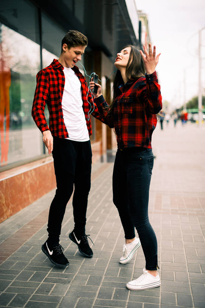 Dos felices amigos adolescentes de moda caminando y bailando en la ciudad, escuchando la música con auriculares, hablando entre sí y sonriendo. Conceptos de estilo de vida, amistad y vida urbana
. - Foto, Imagen