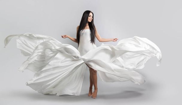 beautiful young girl in flying white dress. Flowing fabric. Light white cloth flying in the wind - Foto, immagini
