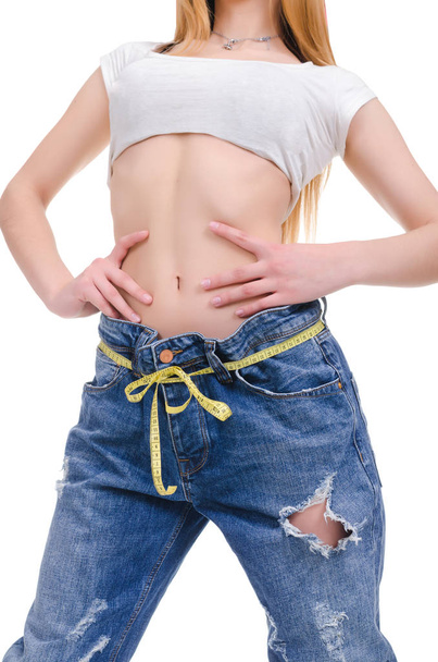  Dieta. Fitness. Chica joven en pantalones vaqueros azules de gran tamaño sobre un fondo blanco
 - Foto, imagen