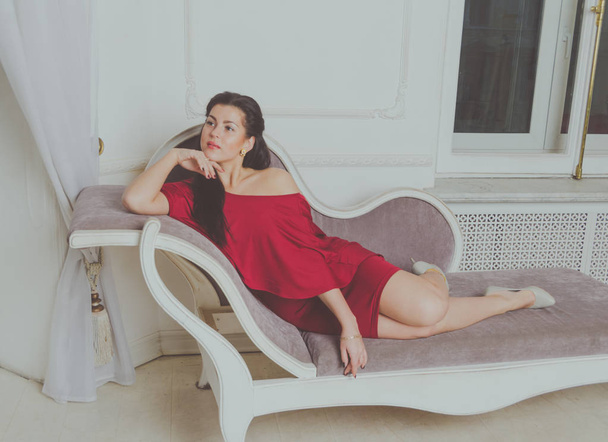  on the couch beautiful girl in a red dress - Foto, Imagen