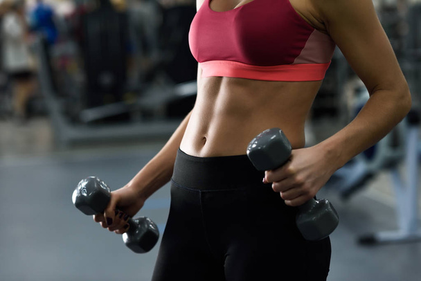 Young woman with beautiful abdomen lifting dumbells at gym - Photo, Image