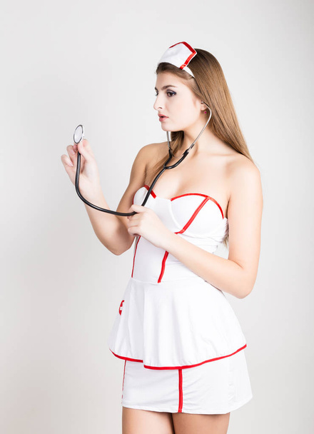 Beautiful smiling sexy nurse standing and holding stethoscope - Zdjęcie, obraz