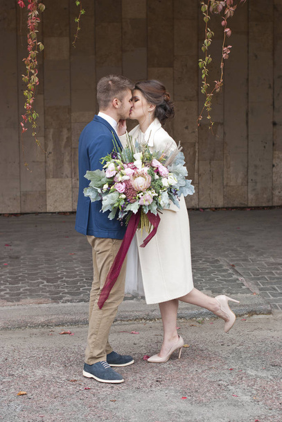 Just married loving couple in wedding dress and suit outdoor in city setting against wall. Happy bride and groom laughing and kissing. Romantic Married young family. - Photo, Image