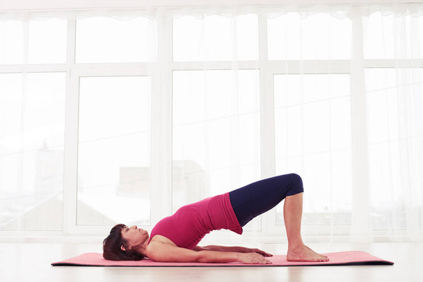 Vrouw doet Turnen de brug pose op een roze yoga mat - Foto, afbeelding