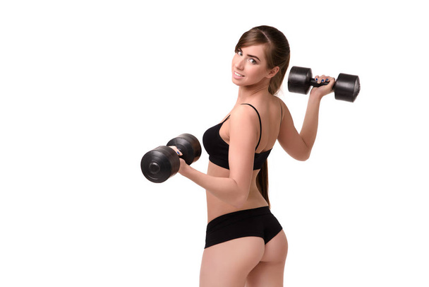 Girl with a beautiful figure shows the ass in  bikini. She is holding the dumbbells back to the viewer - Foto, Imagem