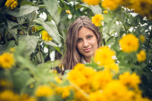 Mädchen spielt Versteck in Ringelblumen und blickt in Nahaufnahme in die Kamera. - Foto, Bild