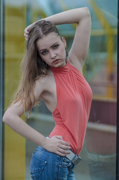 Young beautiful blonde girl in a red summer blouse and jeans posing flexible - Fotó, kép