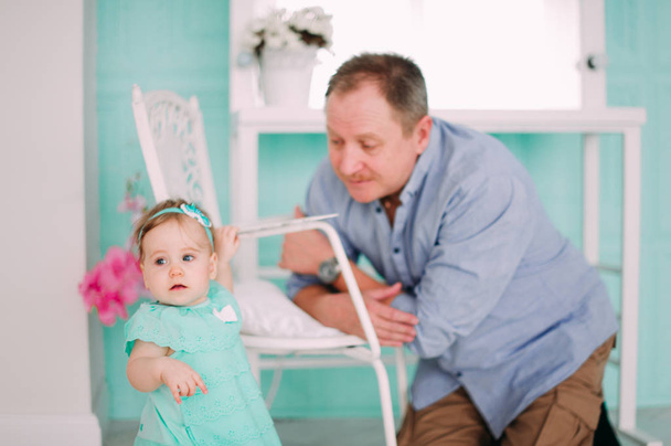 Porträt eines Großvaters im blauen Hemd mit seiner kleinen hübschen Enkelin, die ihn umarmt und aufmerksam zuhört, Studioaufnahme - Foto, Bild