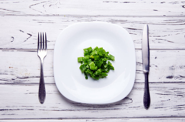Een beetje gehakte groene ui ligt op een groot wit bord. Persoon die lijdt aan anorexia dieet. Veel van de vitaminen in porties van voedsel. De bron van vitamine C. - Foto, afbeelding