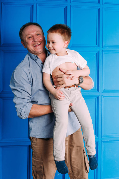 Laughing avô com seu neto como eles brincam juntos dentro de casa na sala de estar com o menino bonito abraçando-o por trás
 - Foto, Imagem