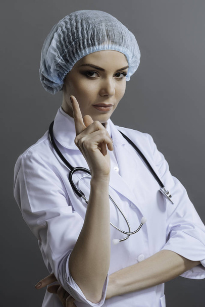 Female doctor gesturing with her finger on grey background - 写真・画像