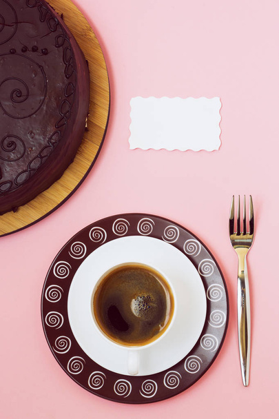 Black coffee whith white card and chocolate cake on pink background - Valokuva, kuva