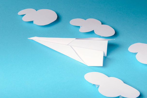 Αεροπλάνο χαρτί στο γυναικείο χέρι πάνω σε μπλε φόντο με σύννεφα - Φωτογραφία, εικόνα