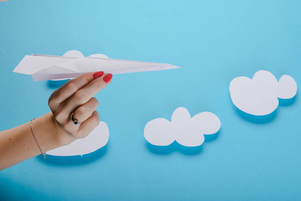 Paper plane in female hand on a blue background with clouds - Φωτογραφία, εικόνα