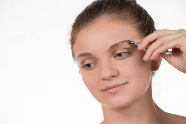 Young girl pulls out her eyebrows with tweezers metal on a white - Foto, Bild